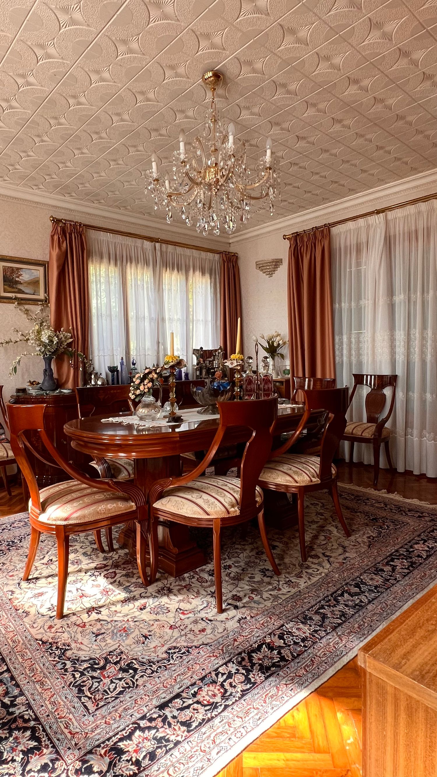 Luxurious dining room with crystal chandelier, ornate ceiling, and traditional wooden furniture on Persian rug.