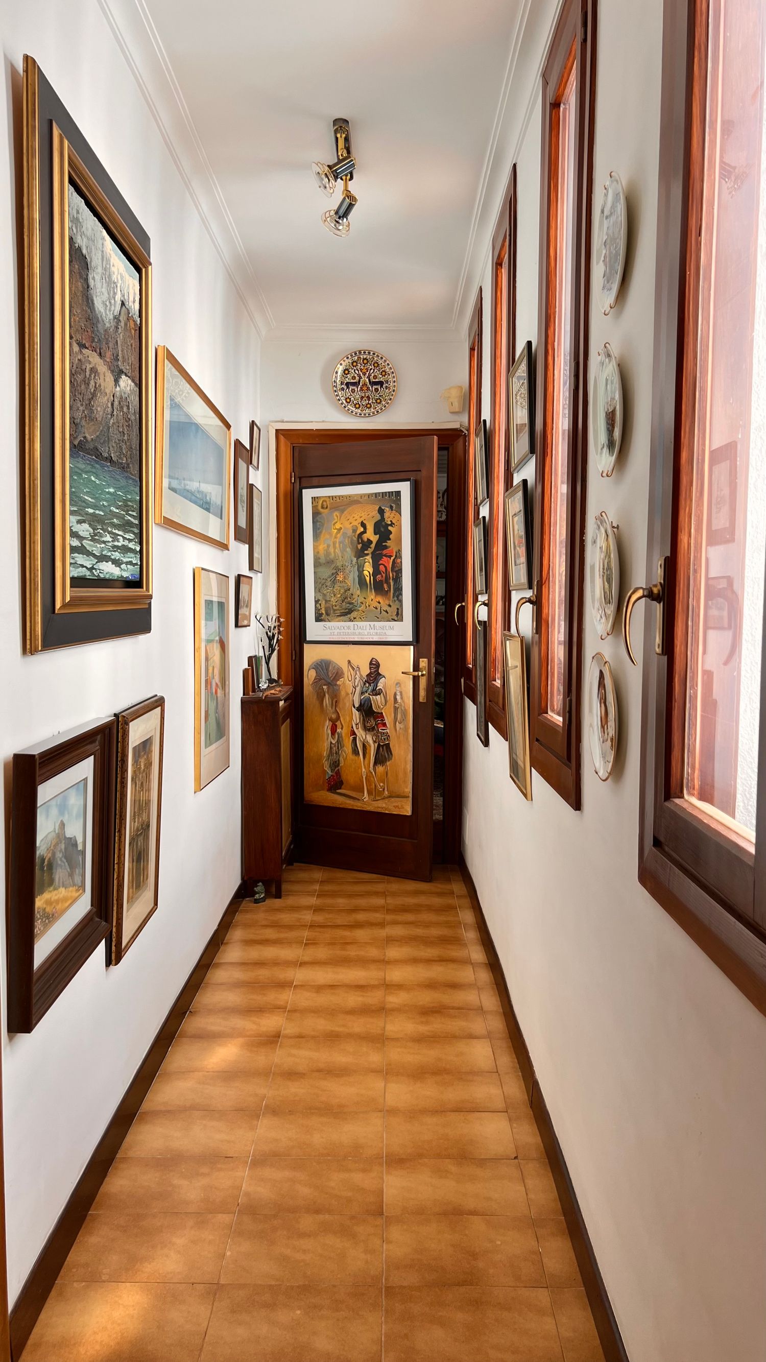 Narrow hallway decorated with framed artwork and landscape paintings on white walls.