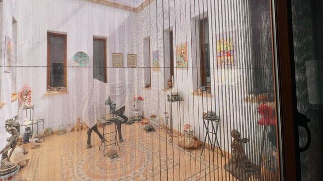 Art gallery corridor with metal sculptures and framed artwork displayed along white walls.