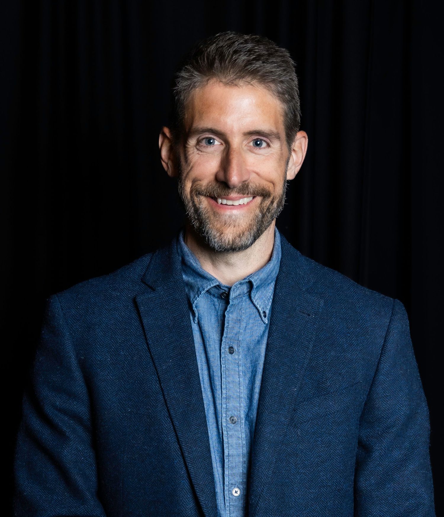 Portrait series featuring navy blazer and light blue button-down shirt against dark backdrop. Headshot