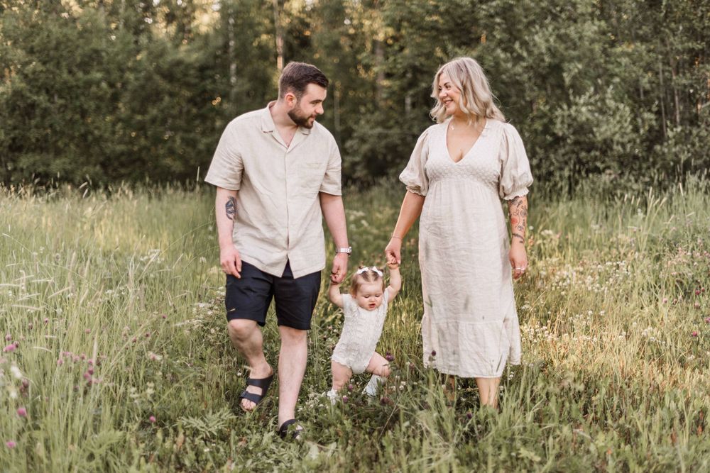 Family walking together through tall grass field at sunset.
