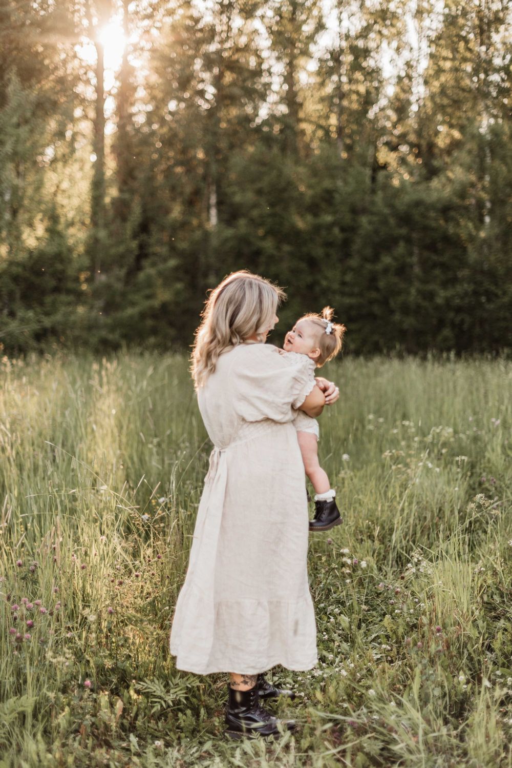 A silhouette of a parent and child in a white dress standing in a sunlit meadow at golden hour.