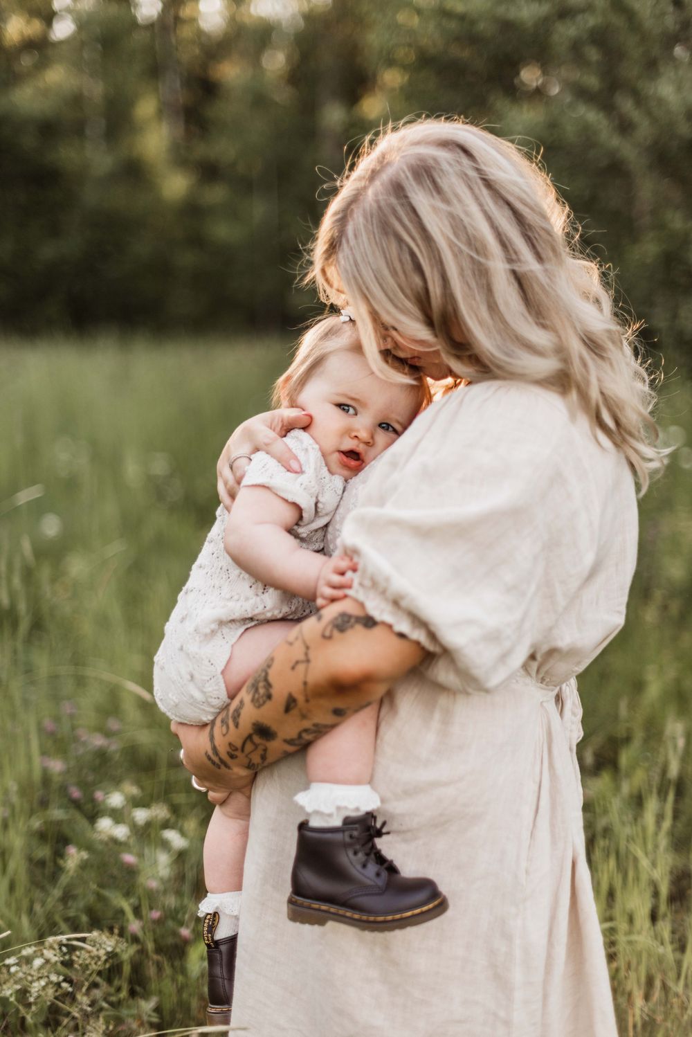 A tender outdoor portrait in a meadow shows an embrace between mother and baby while holding a small boot.