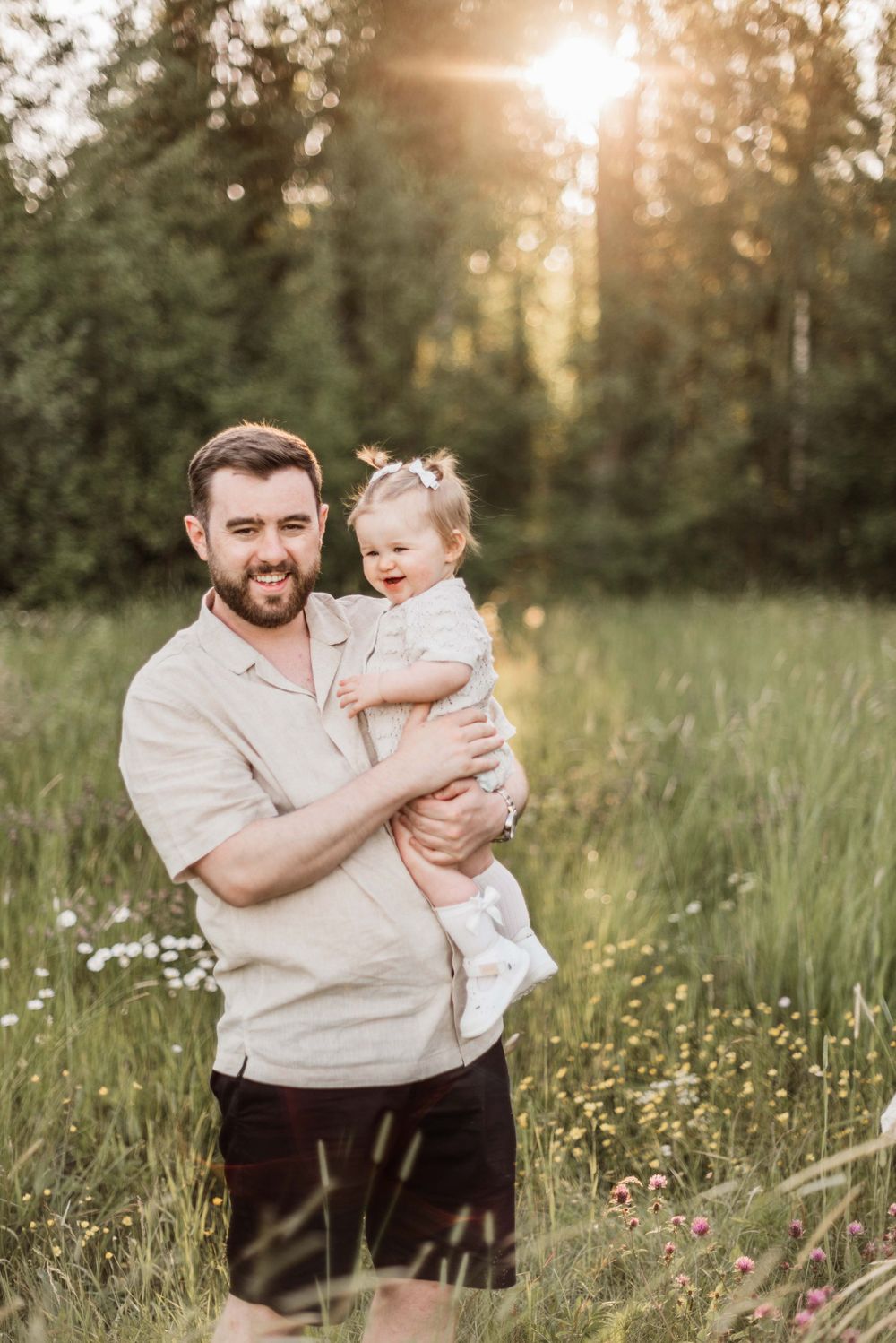A parent and child share a tender moment in a sunlit meadow filled with wildflowers at golden hour. Father.