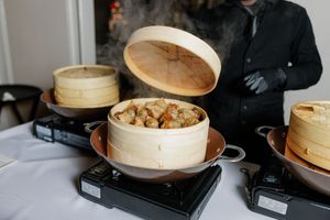 Steam rising from bamboo steamer baskets with savory dumplings at a catered event.