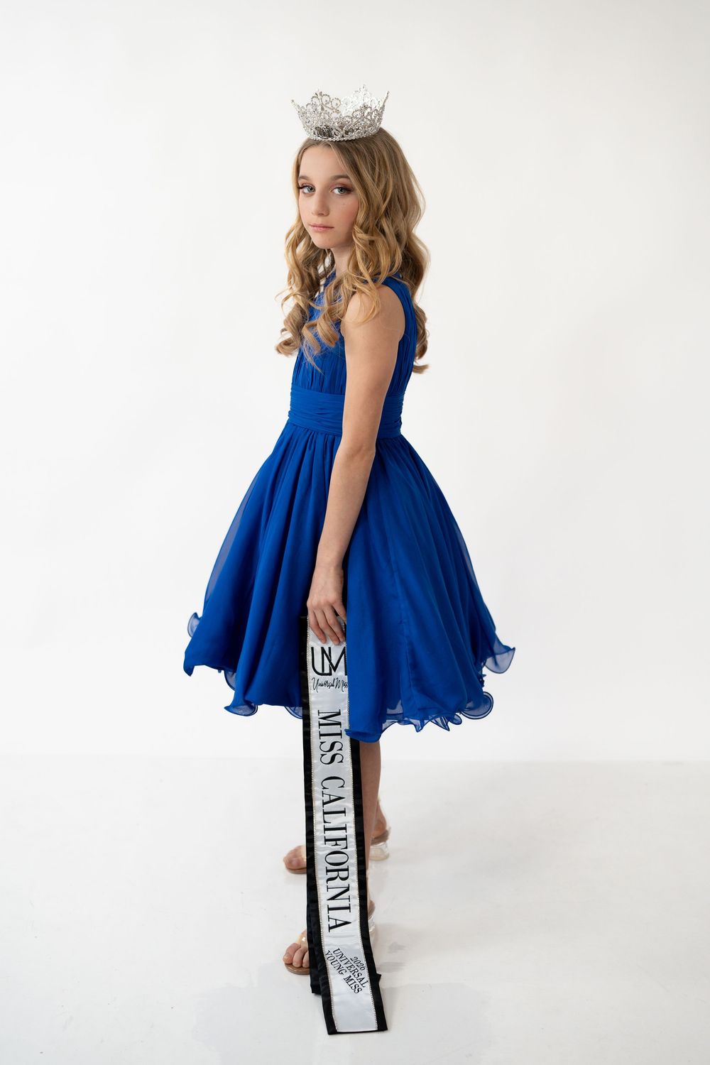 Young girl in royal blue dress poses with books in white studio setting.