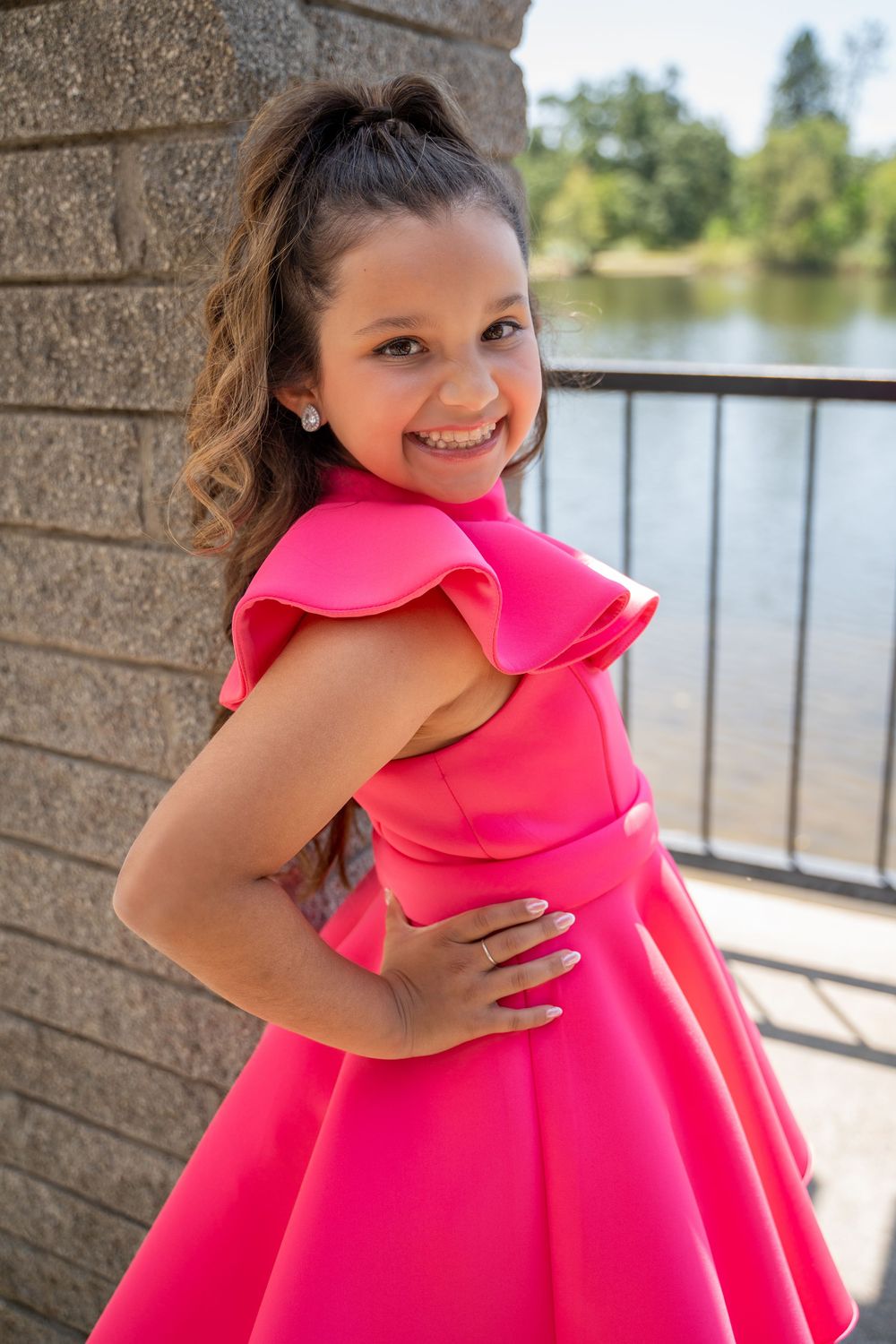 A bright hot pink dress with ruffle details and full skirt photographed by a lake on a sunny day.