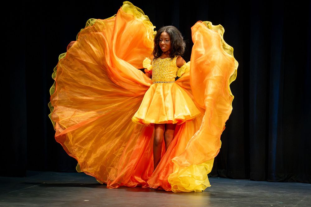 A performer in a flowing orange dress twirls gracefully on stage during a dramatic dance performance.