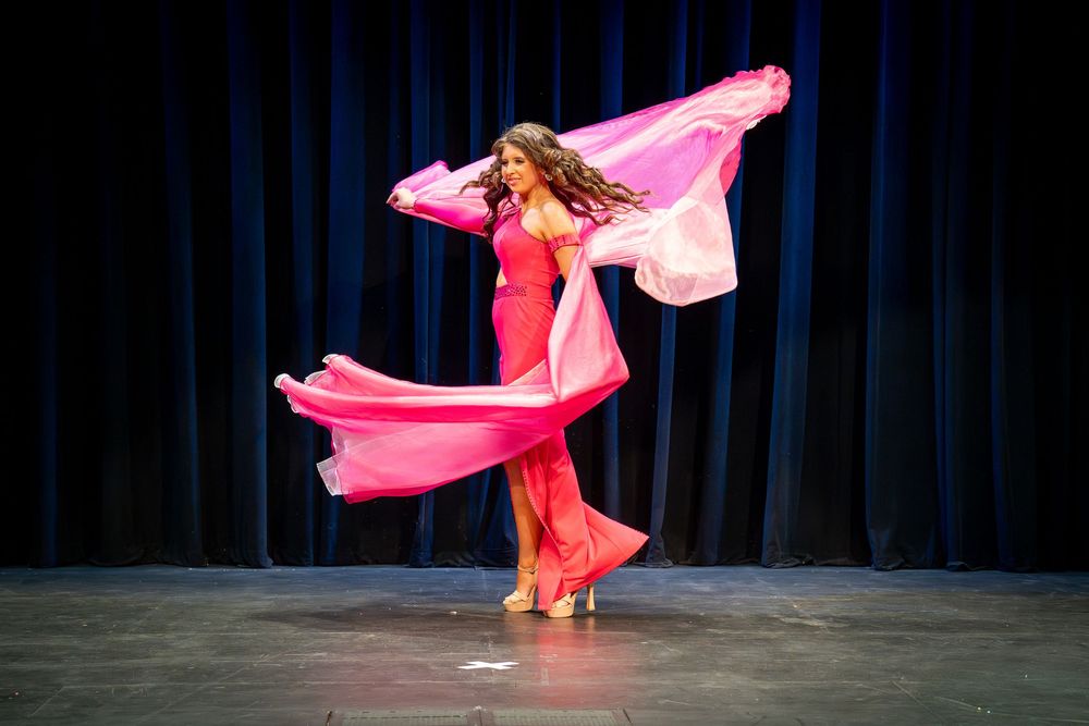 A dancer in a vibrant pink dress spins dramatically on stage with flowing fabric creating elegant movement.