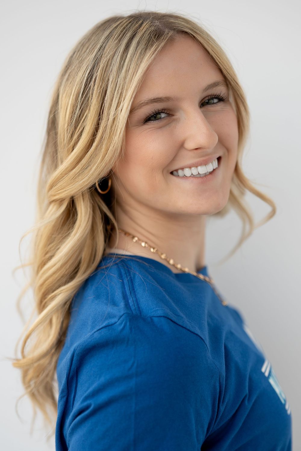 Smiling blonde woman in a blue top with gold necklace, posing for a professional headshot photo.