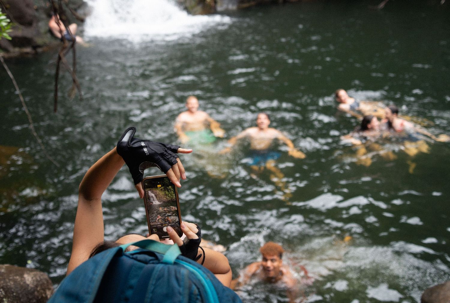 Camera operator films swimmers enjoying a natural waterfall pool.