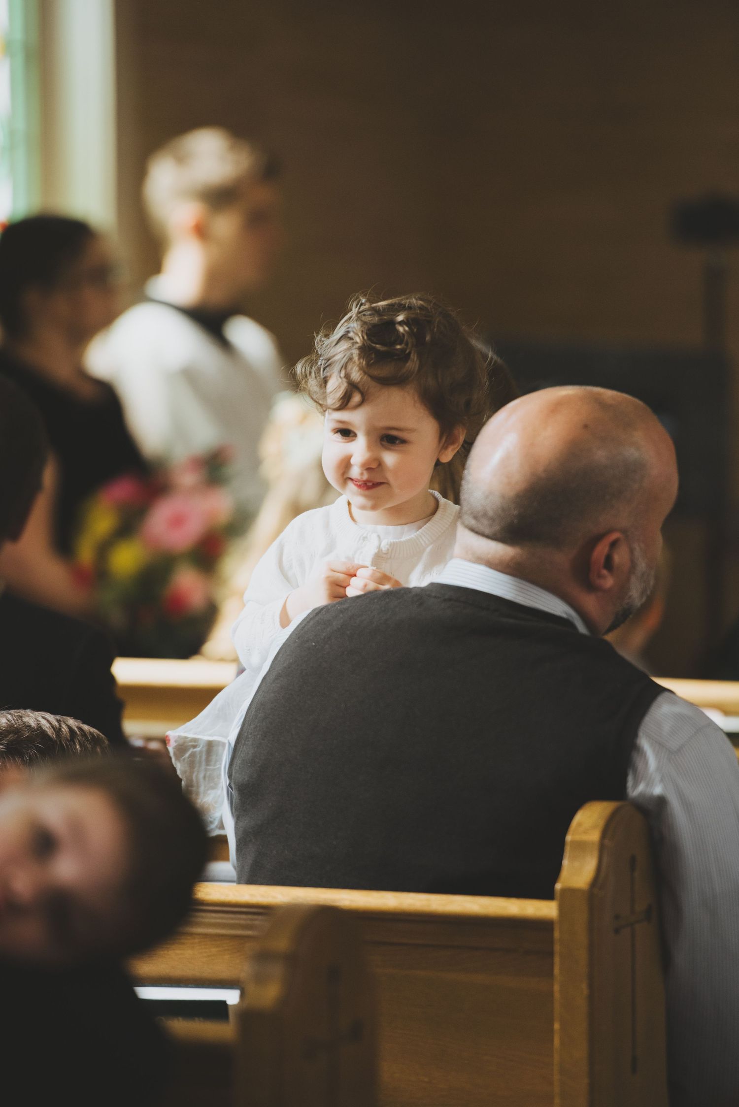 Young child smiling during a church service while sitting in wooden pews.