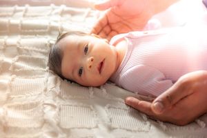 Infant in pink knit clothing lying on white textured blanket.