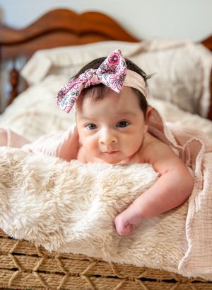 Baby wearing pink bow headband lying on fluffy white rug.