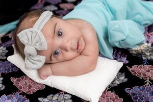 Sleeping infant in white headband lying on patterned bedding with floral design.