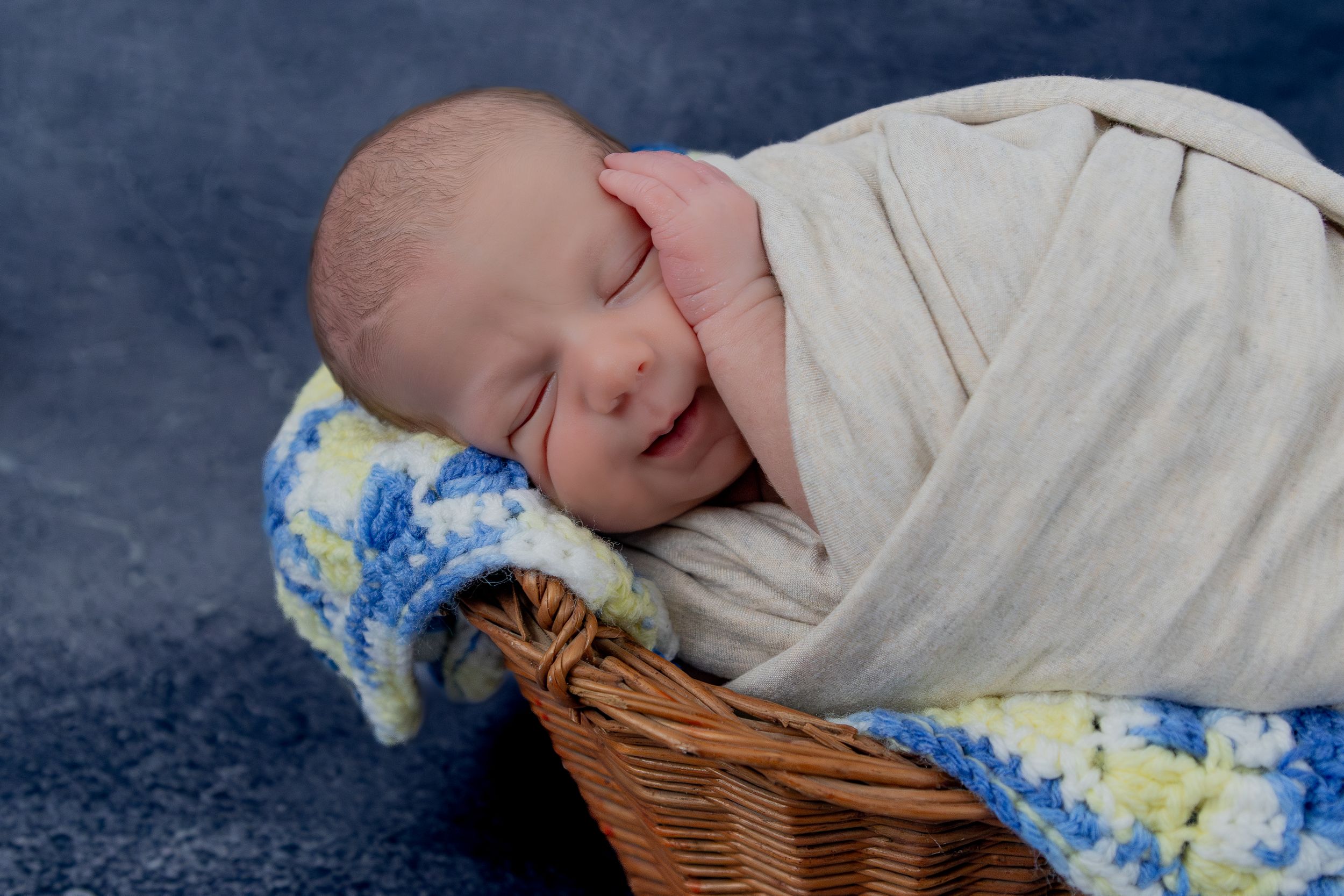 Sleeping newborn wrapped in cream blanket in woven basket.