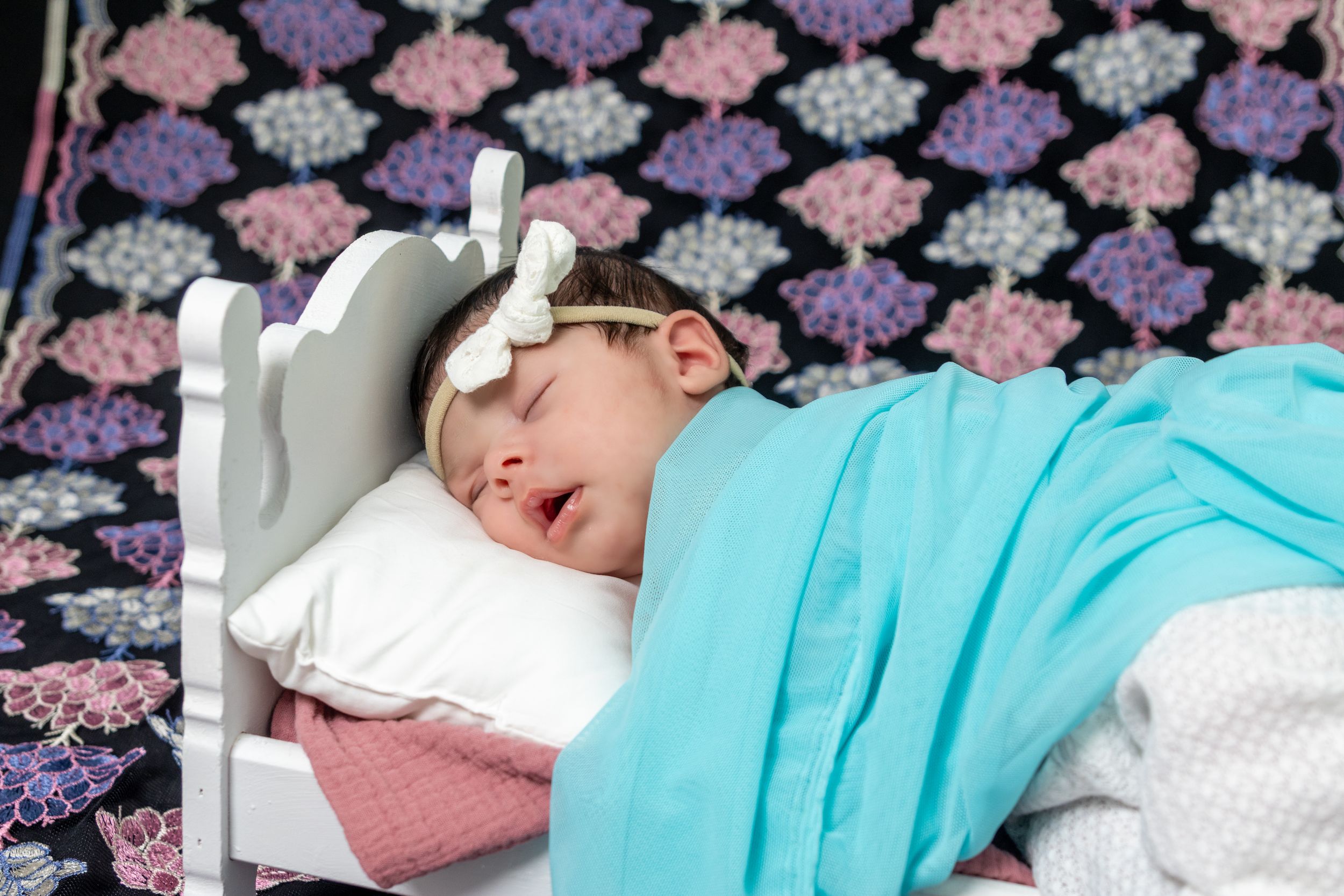 Baby napping on patterned bedding with turquoise blanket.