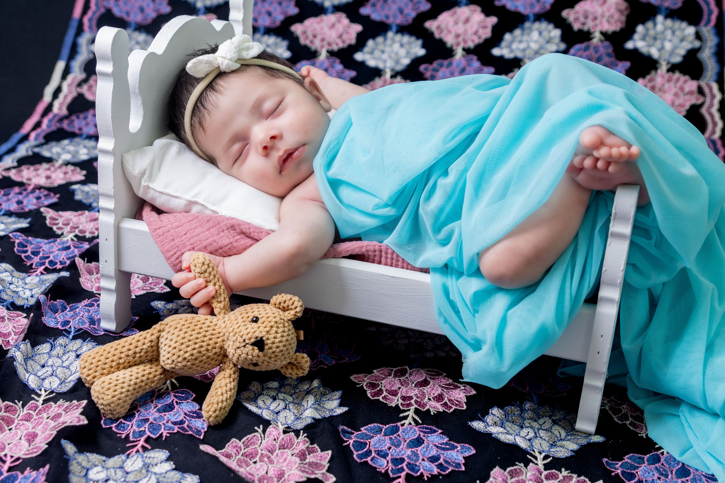 Sleeping baby with teddy bear on floral print bedding.