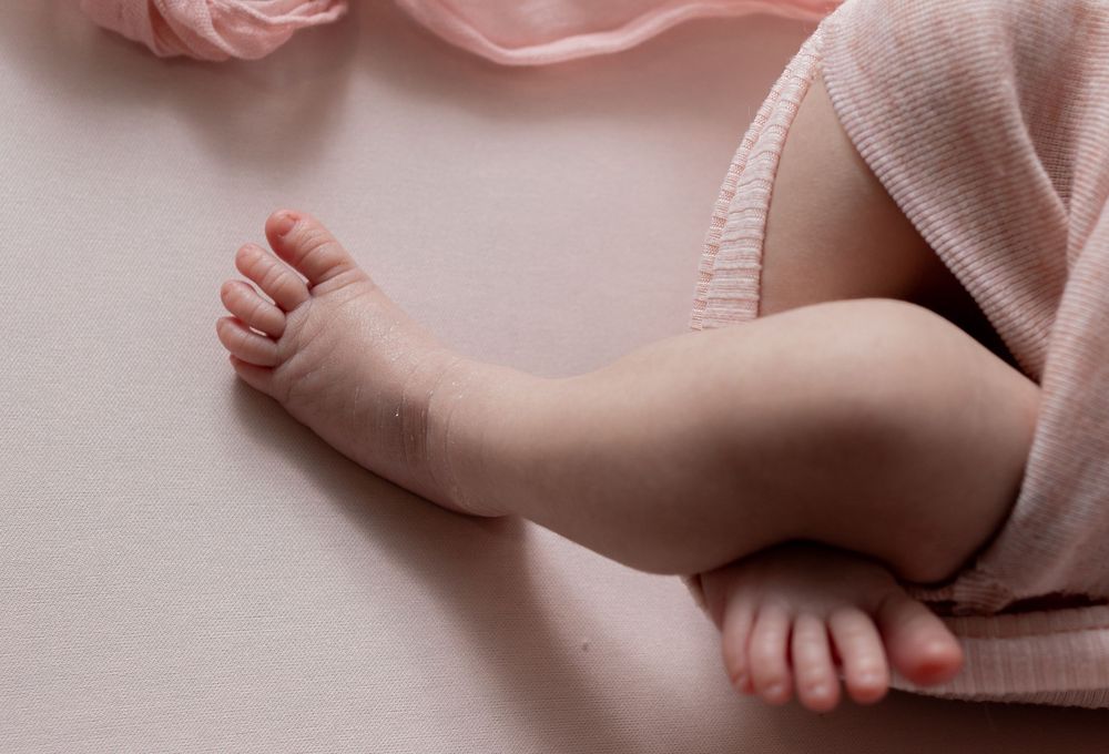 Close-up of tiny baby feet and legs wrapped in a soft pink knit blanket on a light background.