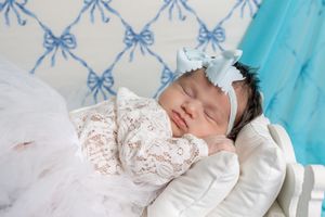 Sleeping newborn baby girl in lace outfit with blue bow headband on white pillow with blue bow wallpaper.