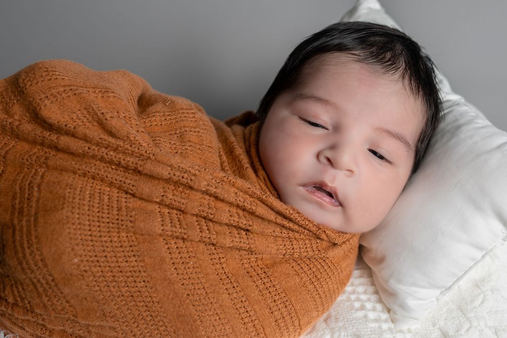 Newborn baby swaddled in a warm orange knit blanket, sleeping peacefully on a white pillow.