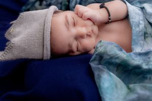 Sleeping infant wearing a knit hat on blue fabric.