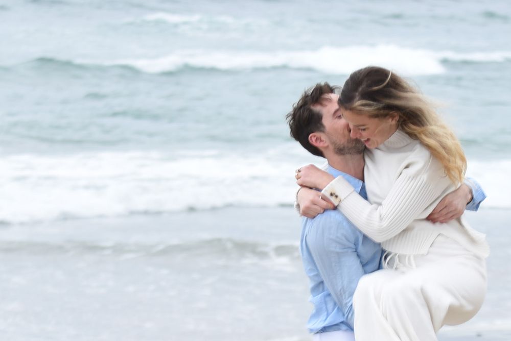 A romantic moment shared between a couple on a misty beach with ocean waves behind them.