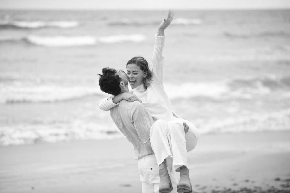 A black and white photo of a joyful beach embrace with crashing waves in the background.