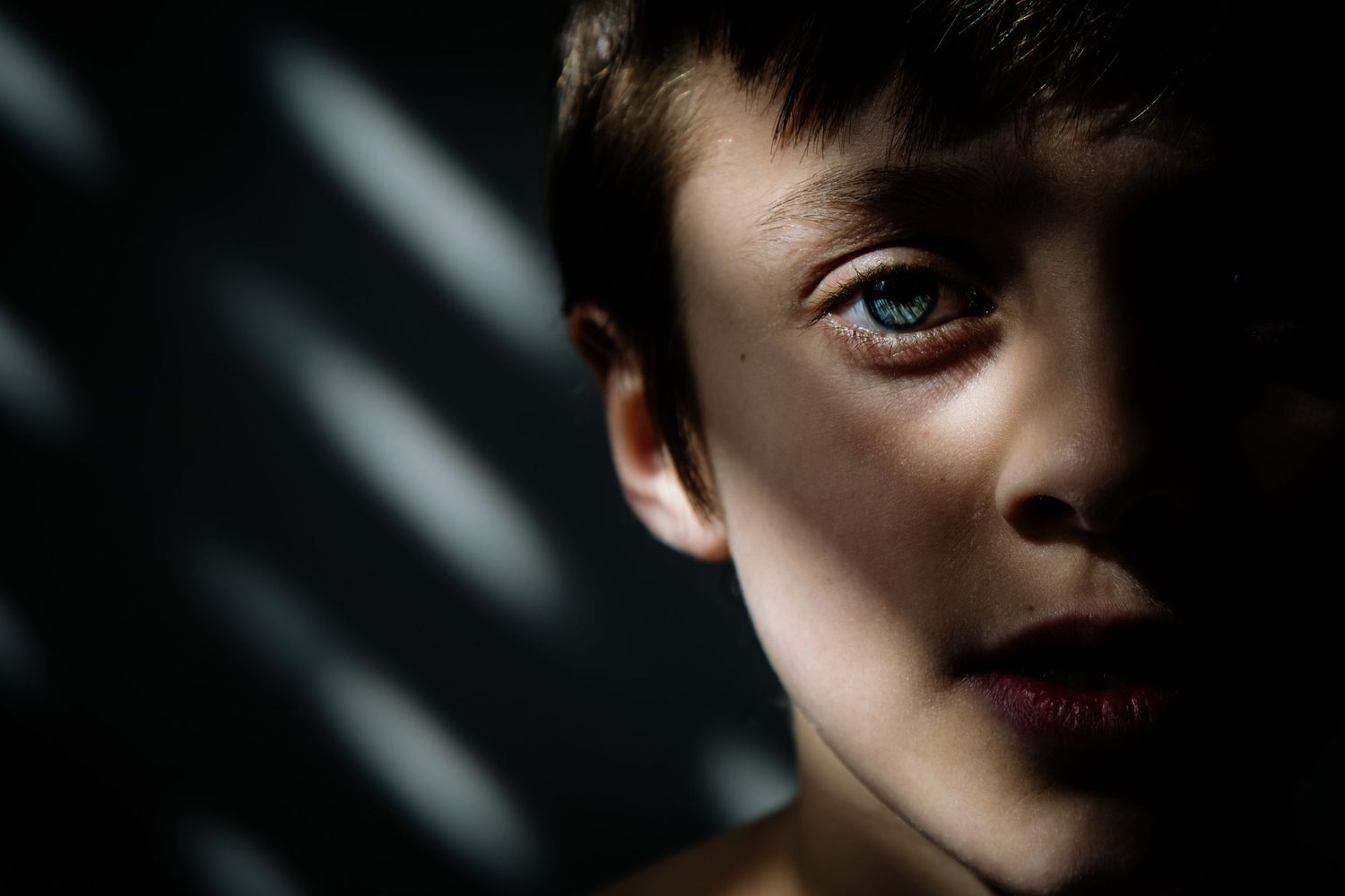 Dramatic close-up portrait with shadows casting lines across a face lit from one side.