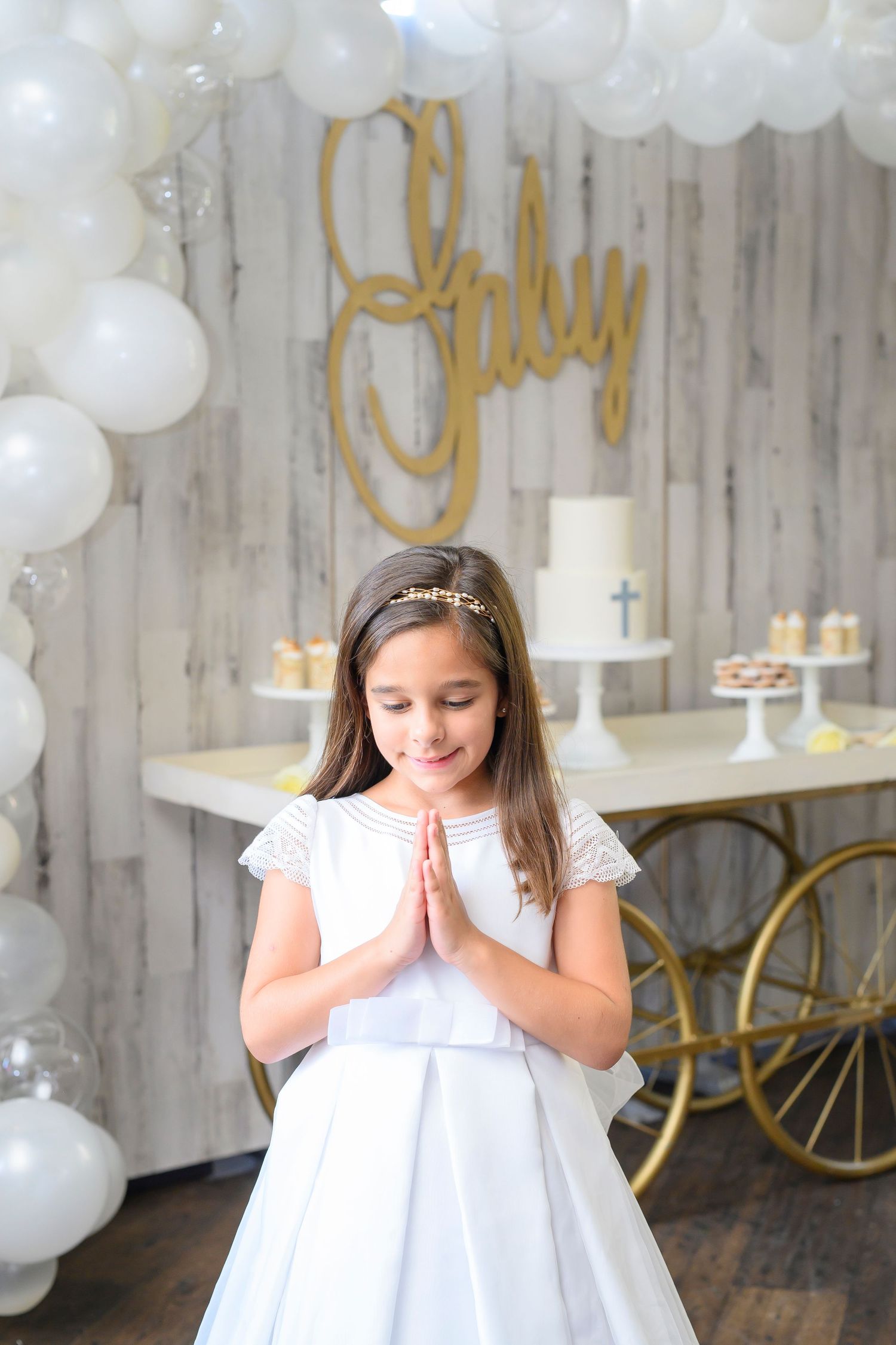 White communion dress and decor with delicate balloon arch and golden accents for special celebration.