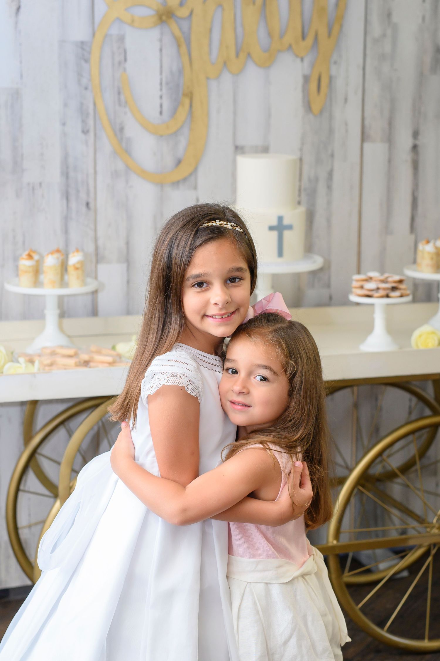 Elegant white communion celebration with balloon arch and dessert display in rustic setting.