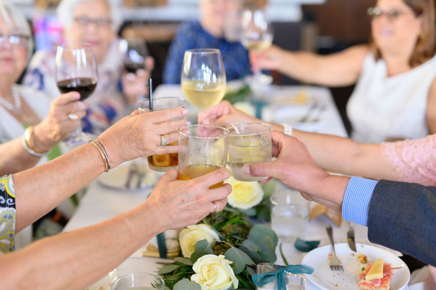 Group toasting with wine glasses over elegant table setting with floral centerpieces.