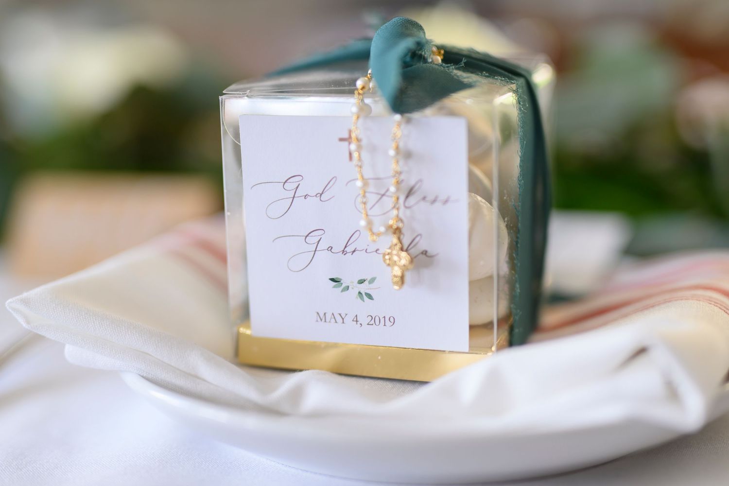 Elegant wedding favor box with calligraphy tag and blue ribbon against white fabric.