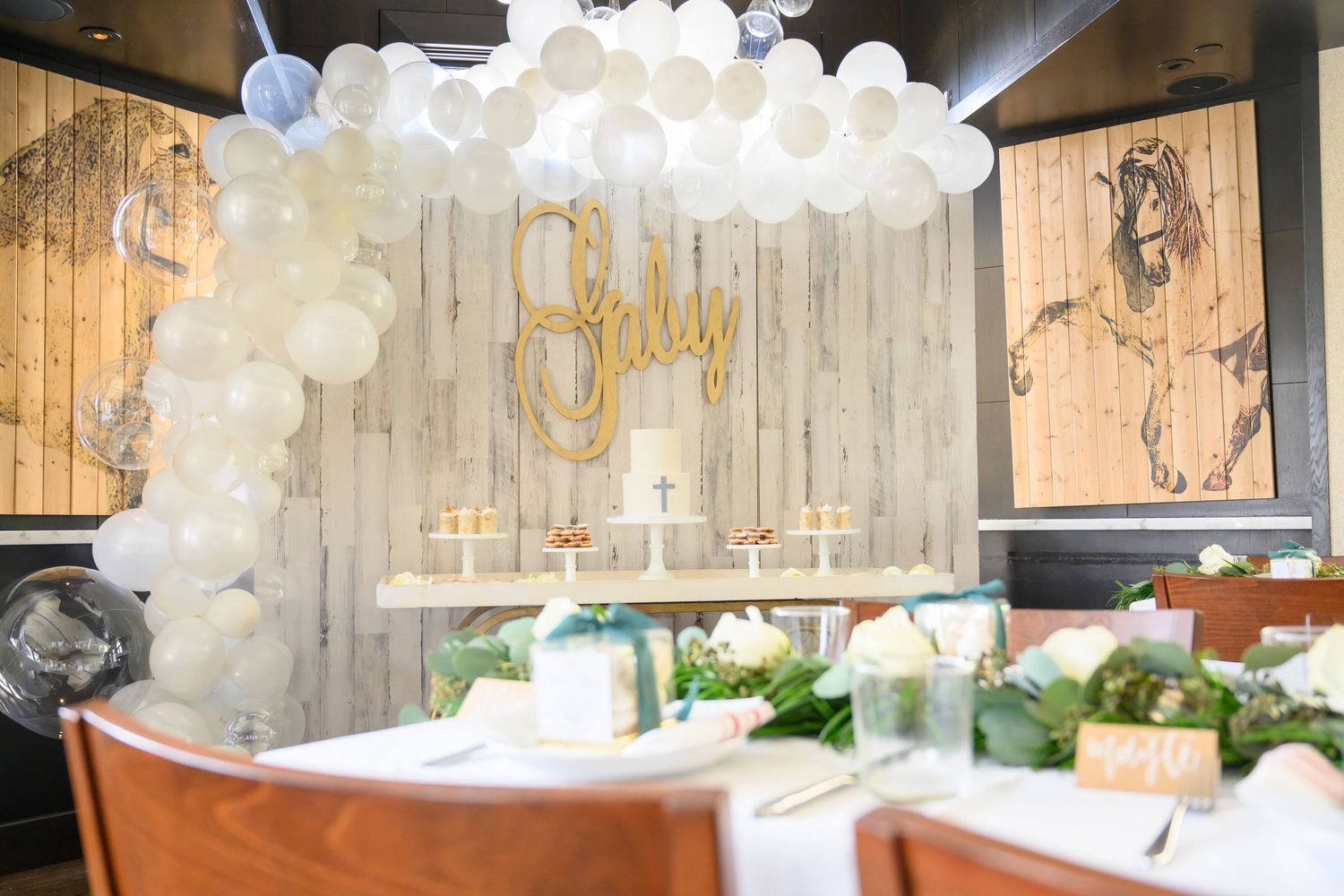 White balloon arch and gold lettering decorate rustic wood panel wall for celebration.