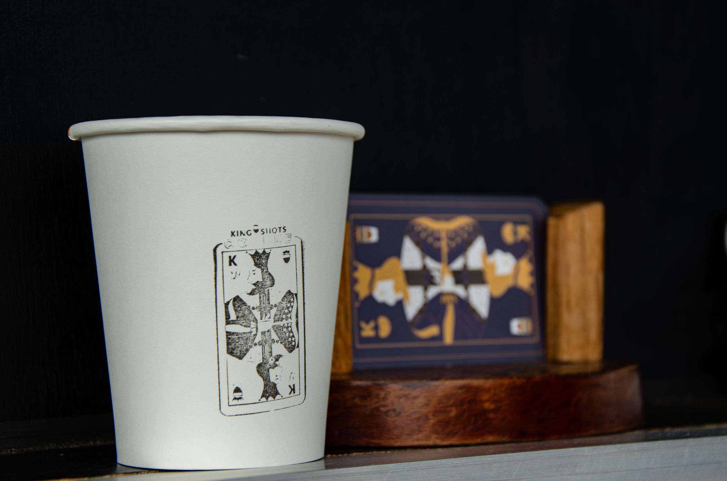 A white coffee cup with playing card design against dark background with decorative box.
