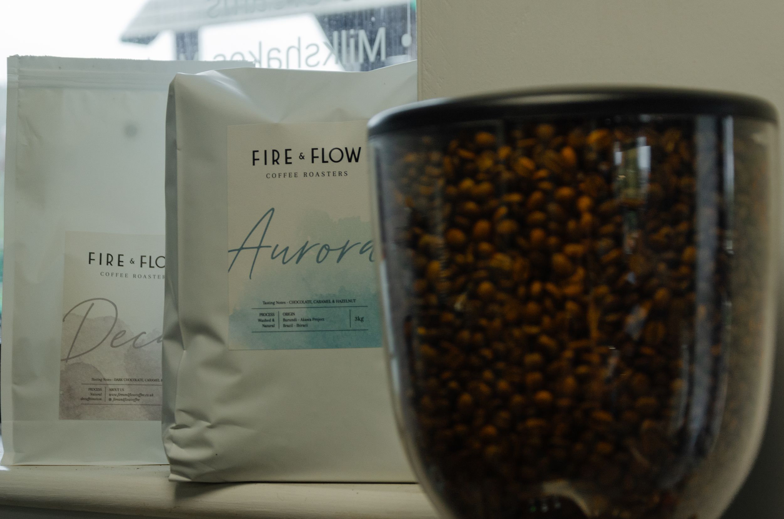 Two bags of Fire+Flow Aurora coffee beans with jar of whole beans in foreground.