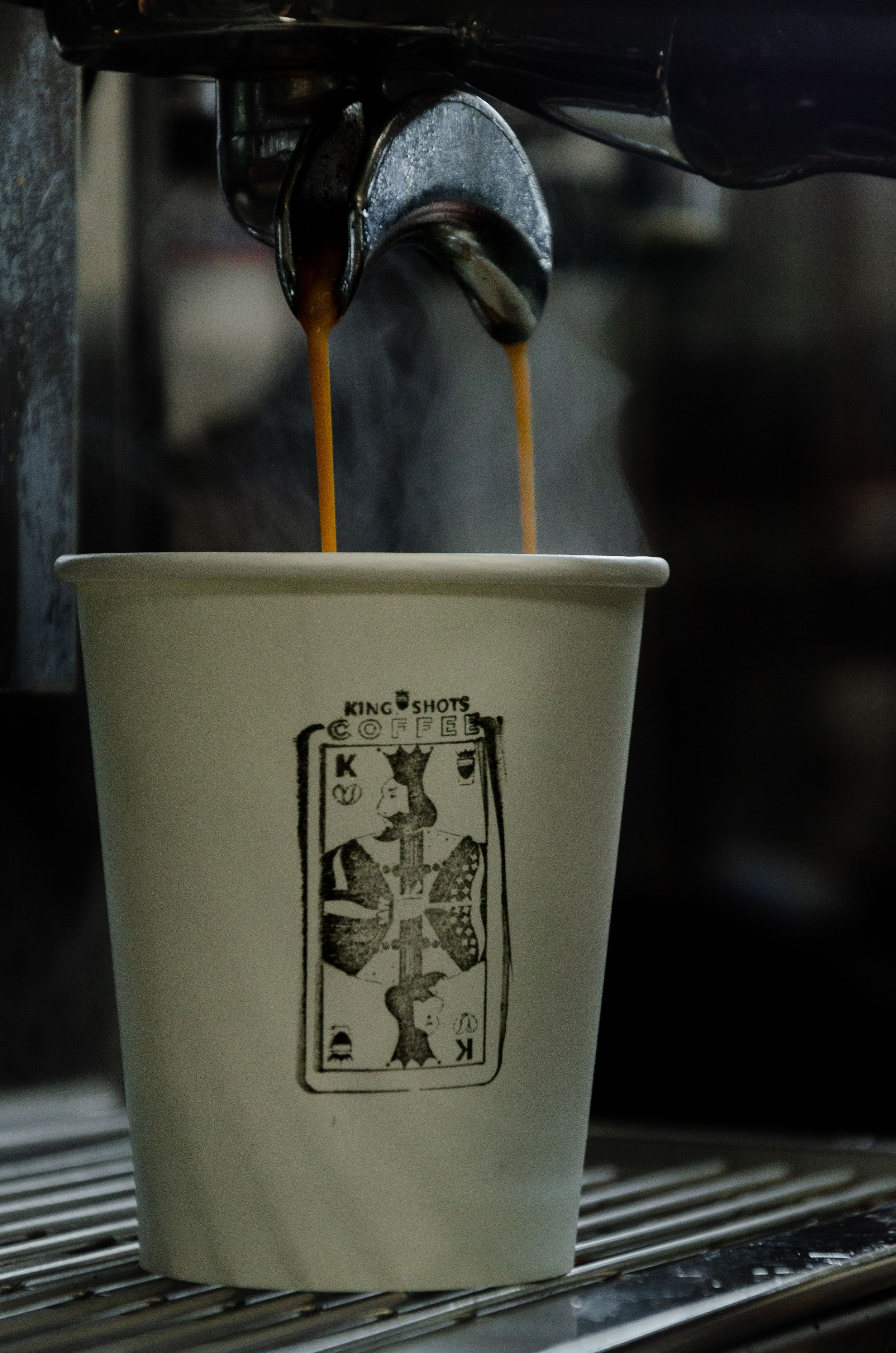 Espresso shot pouring into white paper cup with playing card design.