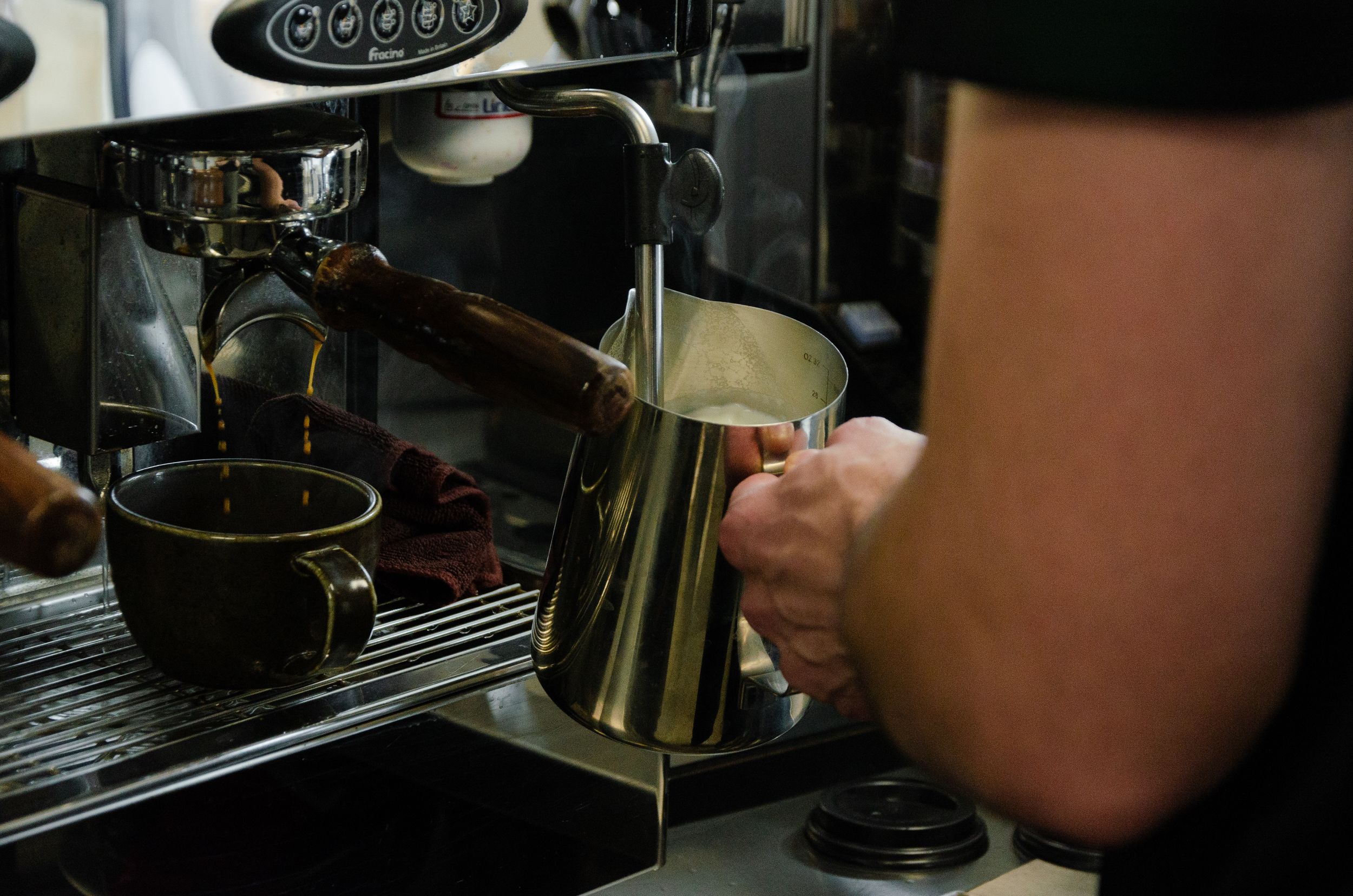 Barista steaming milk in a metal pitcher using an espresso machine.