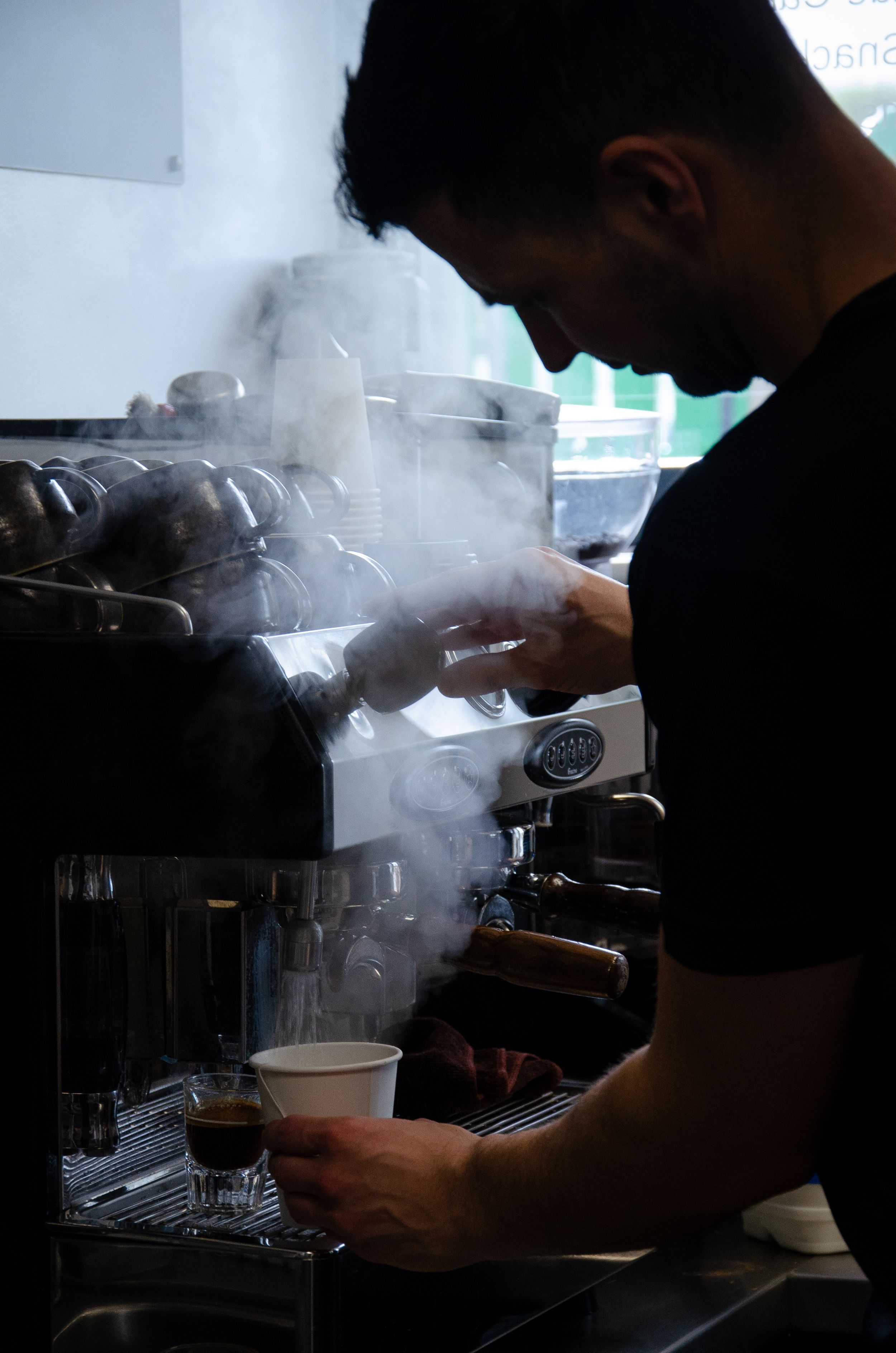 Steam rises as a barista operates an espresso machine in dramatic lighting.