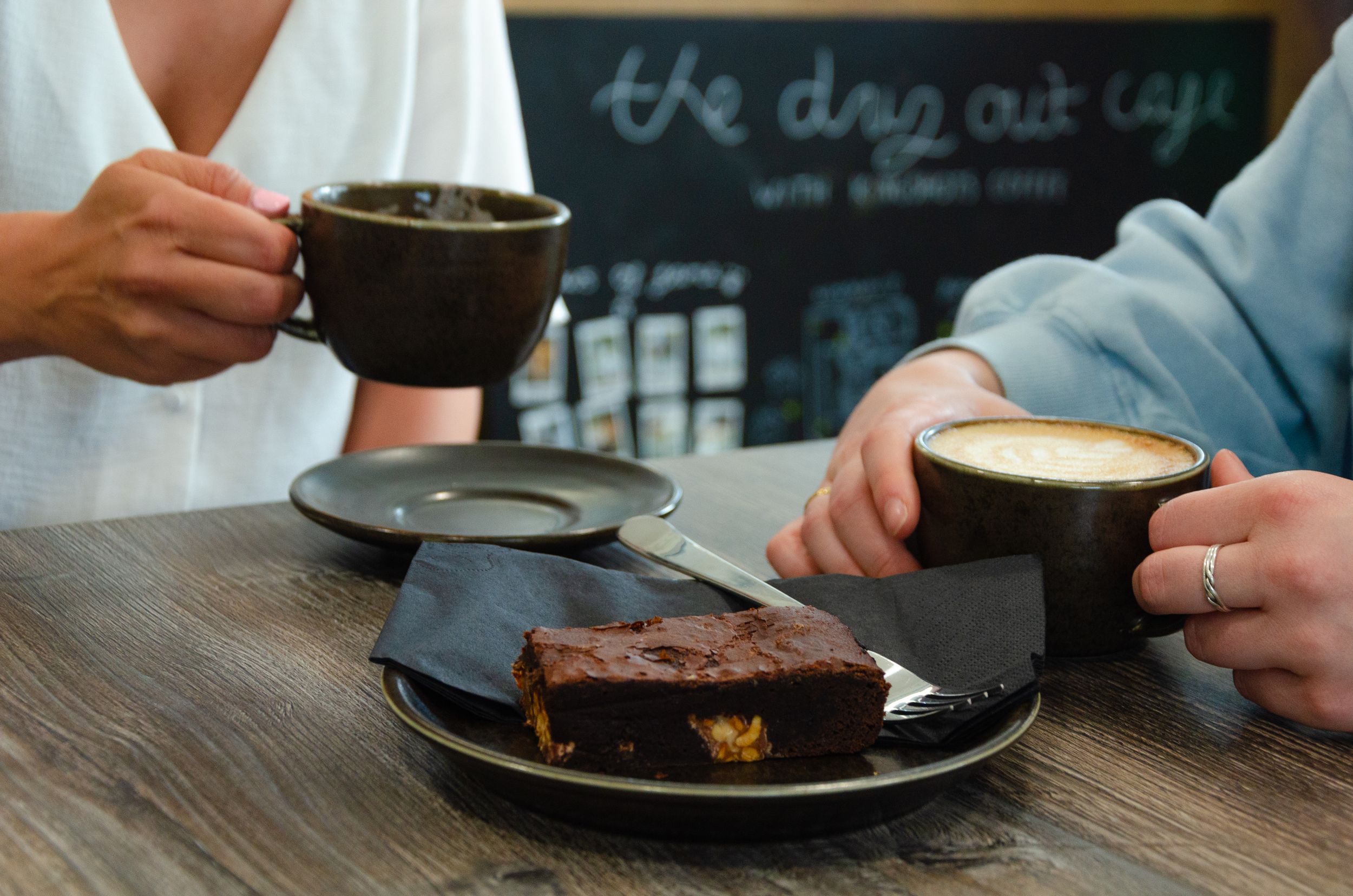 Coffee and chocolate cake being served on dark plates at a cafe table.