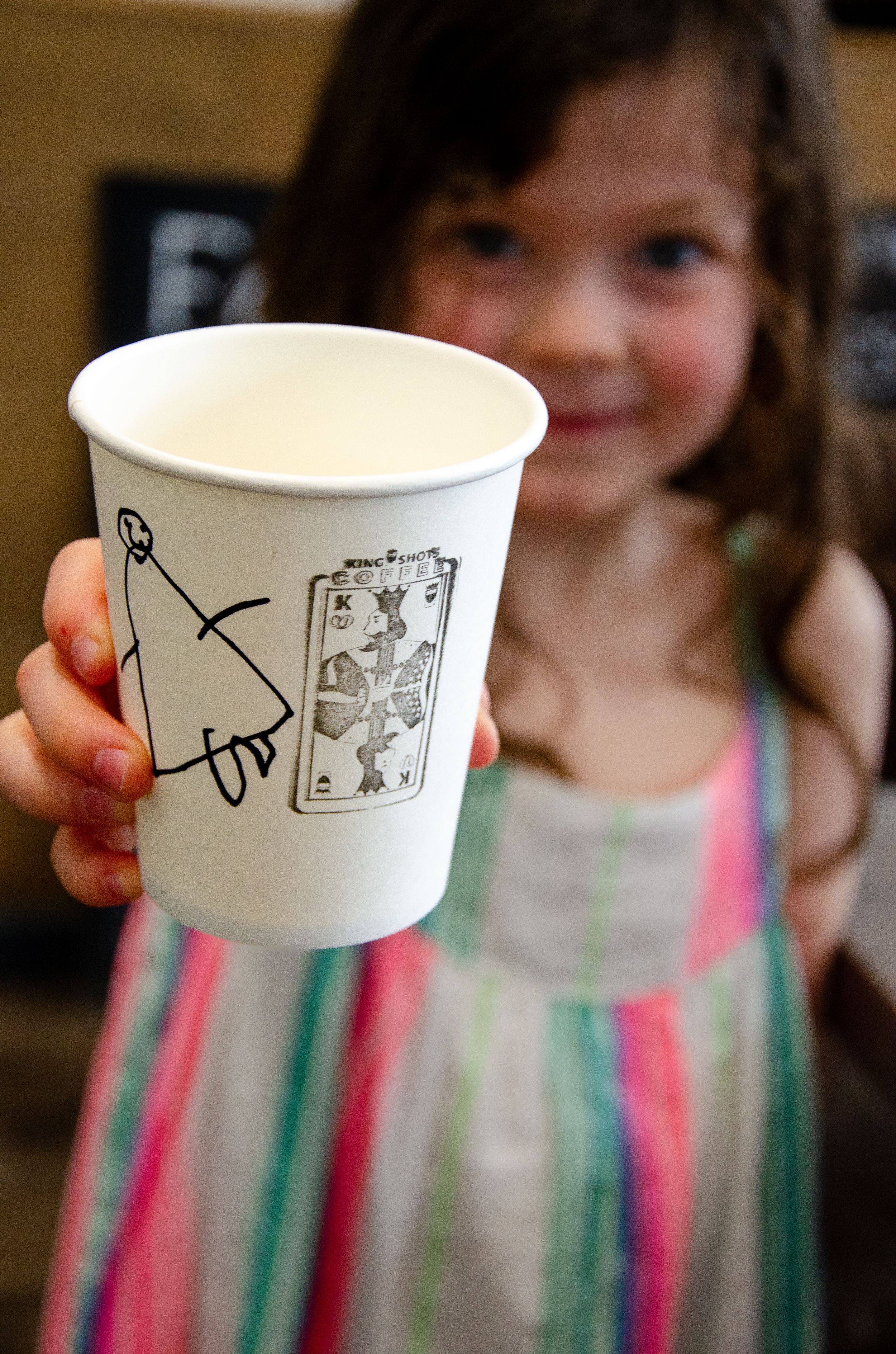 White paper coffee cup with hand-drawn artwork displayed in foreground.