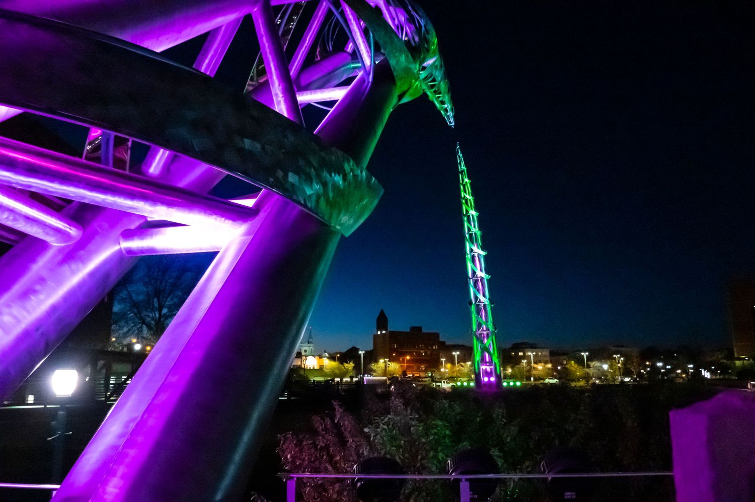 Purple and green illuminated architectural elements against night cityscape.