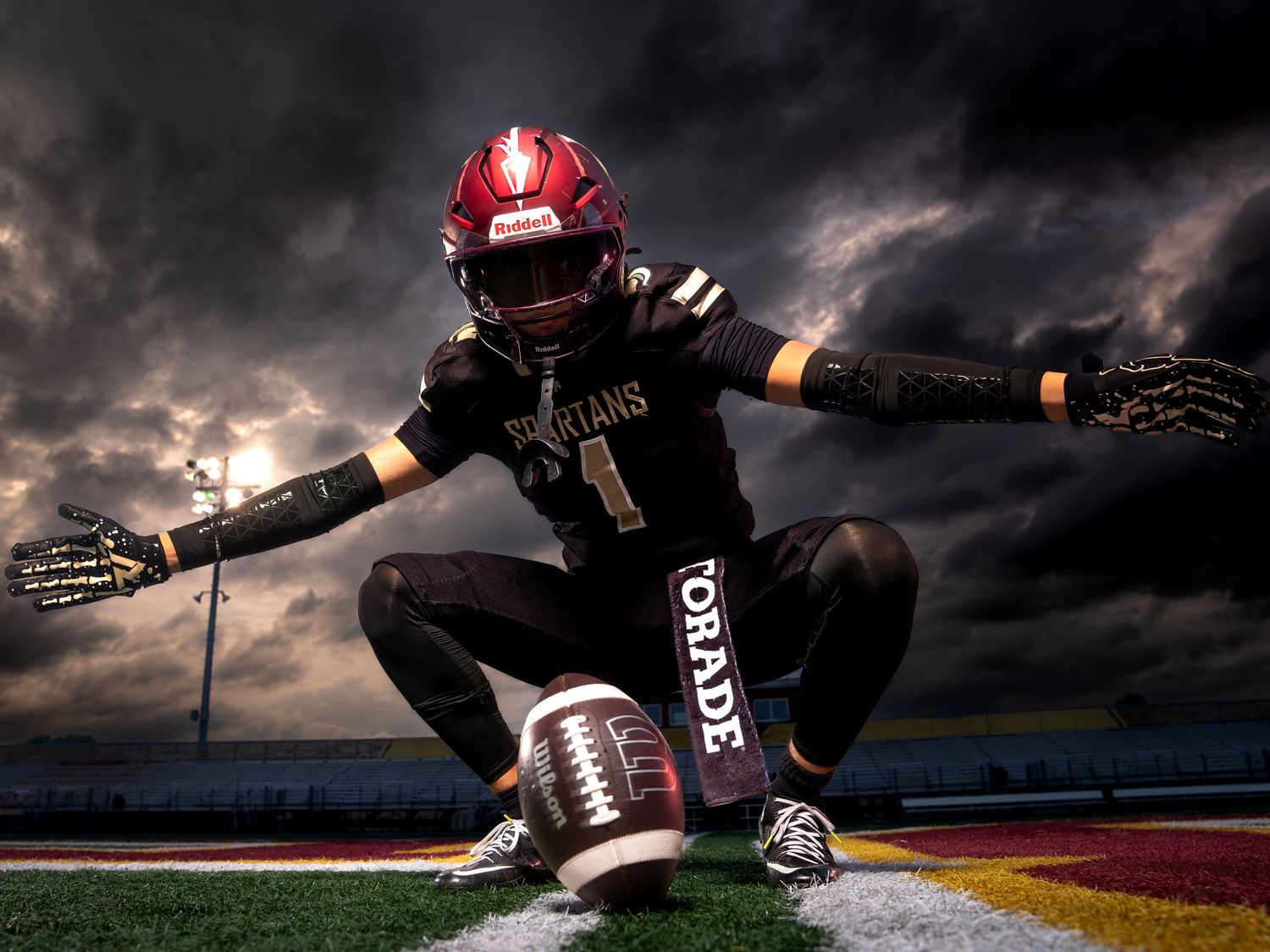 Spartans football player kneels dramatically on field under dark stormy sky.