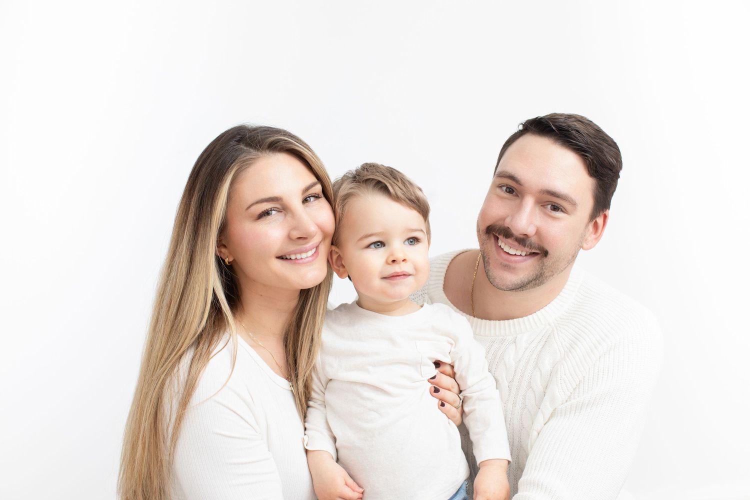 Happy family wearing white poses together against neutral background for a portrait.