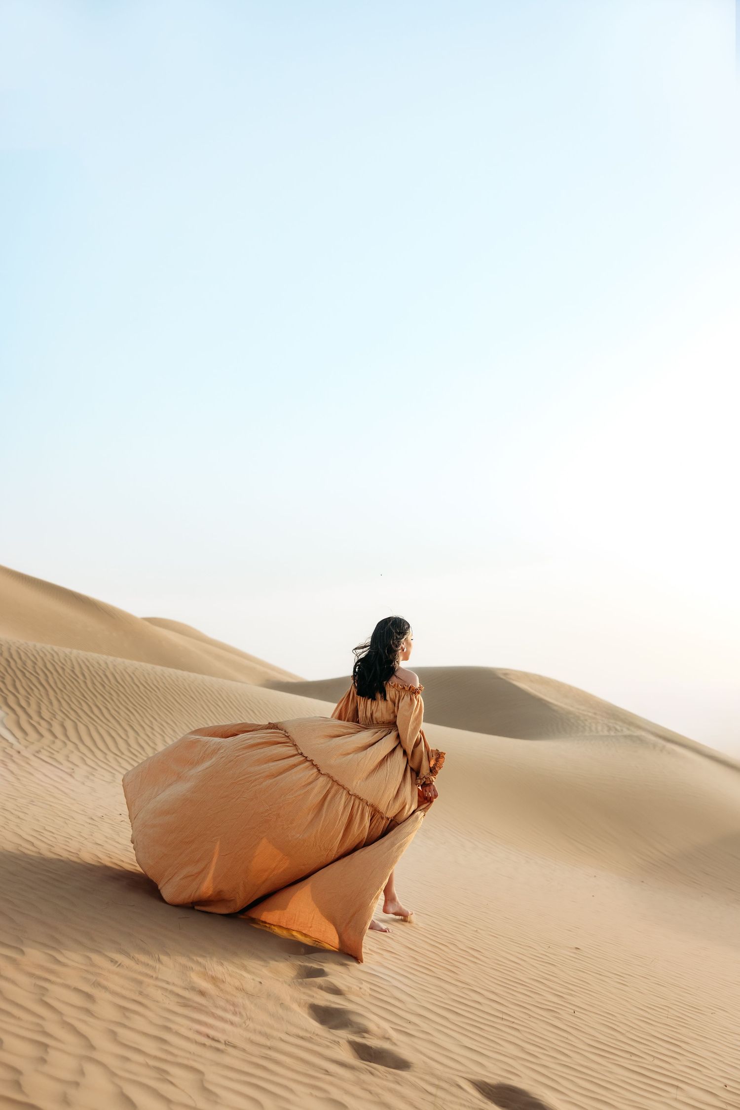A playful family moment on the desert dunes, with parents walking hand-in-hand with their young child, all dressed in white.