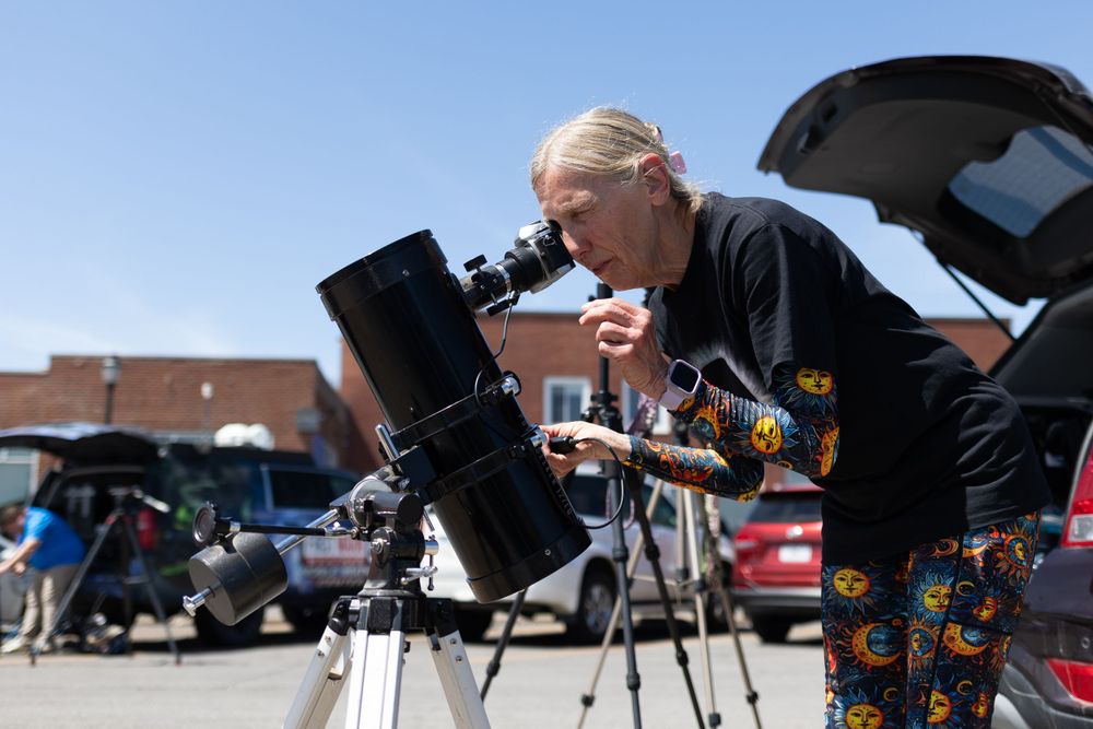 Person using a telescope to observe a solar eclipse in a parking lot.