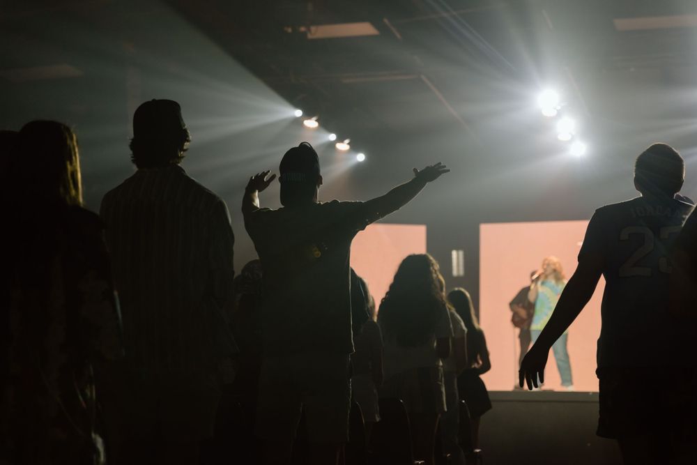 Silhouettes of audience members watching a performance with bright stage lights.