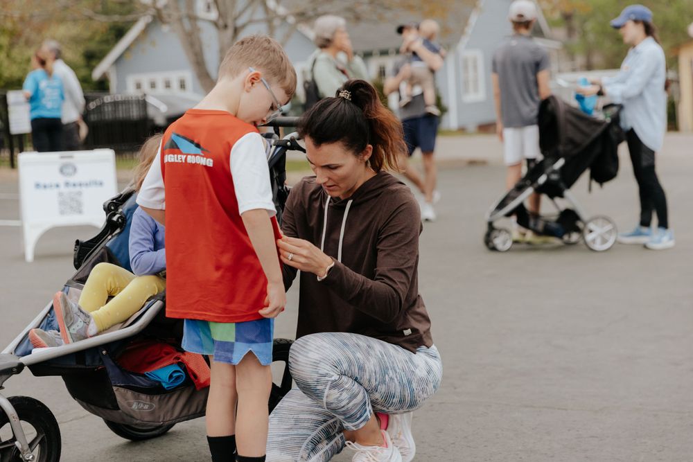 Two people share a moment together on a paved walkway with strollers and pedestrians in the background.