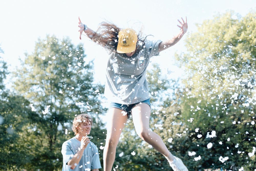 Someone joyfully jumps in the air outdoors on a sunny day with trees in the background.