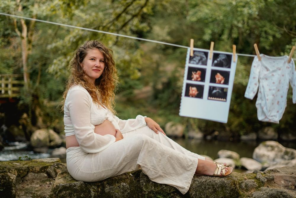 Expectant mother sits outdoors with ultrasound photos and baby clothes on clothesline.